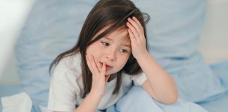 Dengue ou Covid-19: como diferenciar os sintomas em crianças; menina deitada na cama com com uma mão na cabeça e outra no rosto