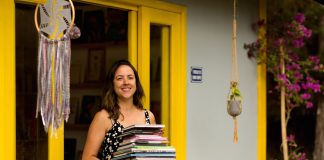 10 dicas de livros de editoras independentes; na foto, Anna Luiza Guimarães, fundadora da Biblioteca Amarela, segura vários livros com as mãos na entrada da biblioteca