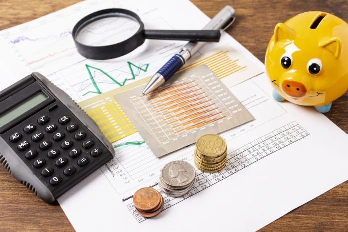 Quer fazer um investimento para seu filho? Invista no seu futuro!; moedas, lupa, caneta, papeis e calculadora sobre mesa