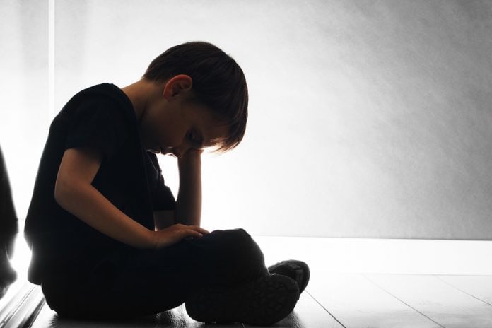 Atitudes que ajudam a identificar a ansiedade nas crianças; menino está sentado, de cabeça baixa apoiada sobre mão