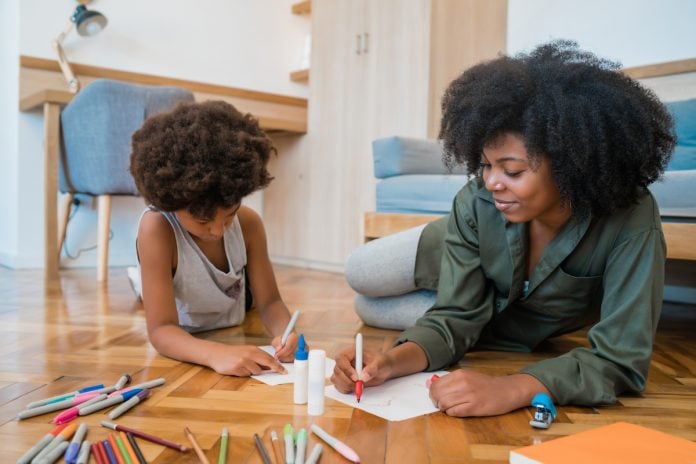 7 princípios que pais e escolas devem ensinar às crianças; deitados no chão, mãe e filho negros fazem desenho sobre papel