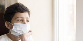 SBP avalia que mortes e hospitalizações por coronavírus em crianças estão em queda; menino com máscara e mão no queixo olha pela janela