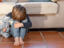 Validar as emoções é acolher a criança quando ela chora _ e não repreendê-la; menino está no chão com cabeça baixa apoiada sobre pernas com joelhos dobrados