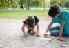 SBP alerta para contaminação de crianças por chumbo; dois meninos desenham com giz no chão em espaço verde ao ar livre