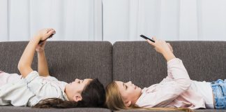 Meninas deitadas no sofá e sorrindo para o celular