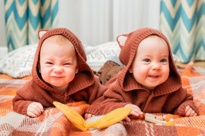 Nascimento de gêmeos atinge níveis sem precedentes, diz estudo; dois bebês gêmeos de capuz marrom, um faz careta e o outro sorri