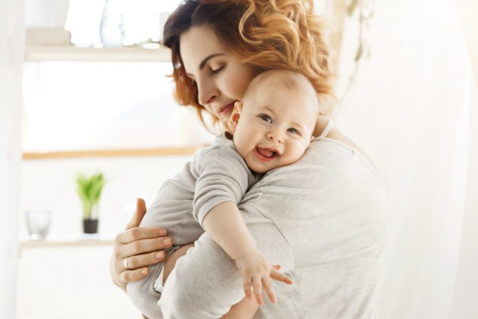 Ptose infantil: saiba como identificar a condição no seu bebê; mãe está abraçada com bebê que encosta rosto sobre seus ombros