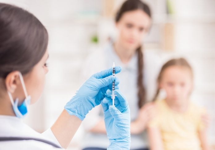 Vacinas contra a covid-19: testes iniciais em crianças têm bons resultados; mulher de luva azul e bata branca segura vacina e ao fundo imagem desfocada mostra criança e mulher adulta