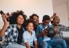 101 coisas para fazer com as crianças antes que eles cresçam; família afro sentada junta no sofá vibra por algo que vê na TV