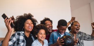 101 coisas para fazer com as crianças antes que eles cresçam; família afro sentada junta no sofá vibra por algo que vê na TV
