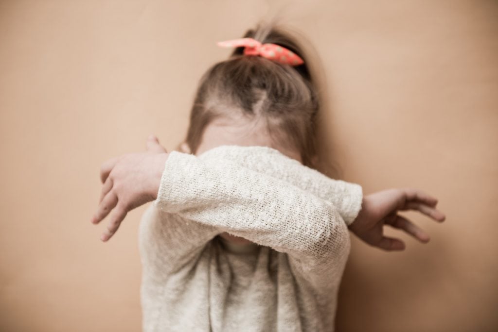 Crianças introvertidas na pandemia: saiba como ajudá-las; menina de cabelo preso cobre rosto com os braços