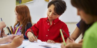 Sensação de pertencimento à escola e suporte emocional da família melhoram desempenho escolar, três alunos escrevem em seus cadernos sobre a mesa