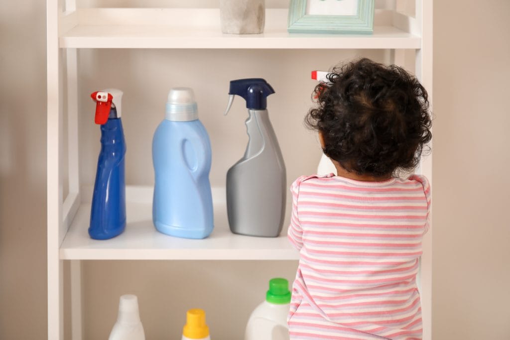 Aprenda como prevenir e proceder em caso de intoxicação de crianças; menino pequeno mexe em produtos de limpeza em prateleira de sua altura
