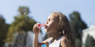 Poluição pode alterar genes de crianças e aumenta risco de doenças cardíacas; menina de cabelo grande brinca de soprar bolhas em espaço ao ar livre