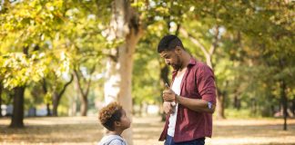 Filhos disciplinados: como chegar ao equilíbrio entre a punição e a permissividade; pai conversa com o filho em meio a parque ao ar livre faz sinal de 'joia' com a mão