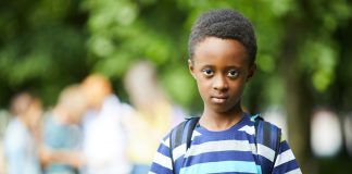Exclusão escolar na pandemia afeta mais as crianças entre 6 e 10 anos; menino negro de mochila nas costas olha fixamente para a câmera