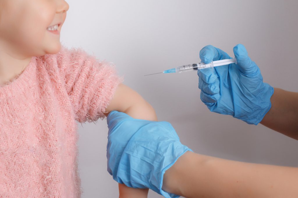 Vacina contra a gripe: qual a importância da vacina para crianças e grávidas ; braço de menina de blusa rosa recebe vacina de um adulto que usa luvas azuis
