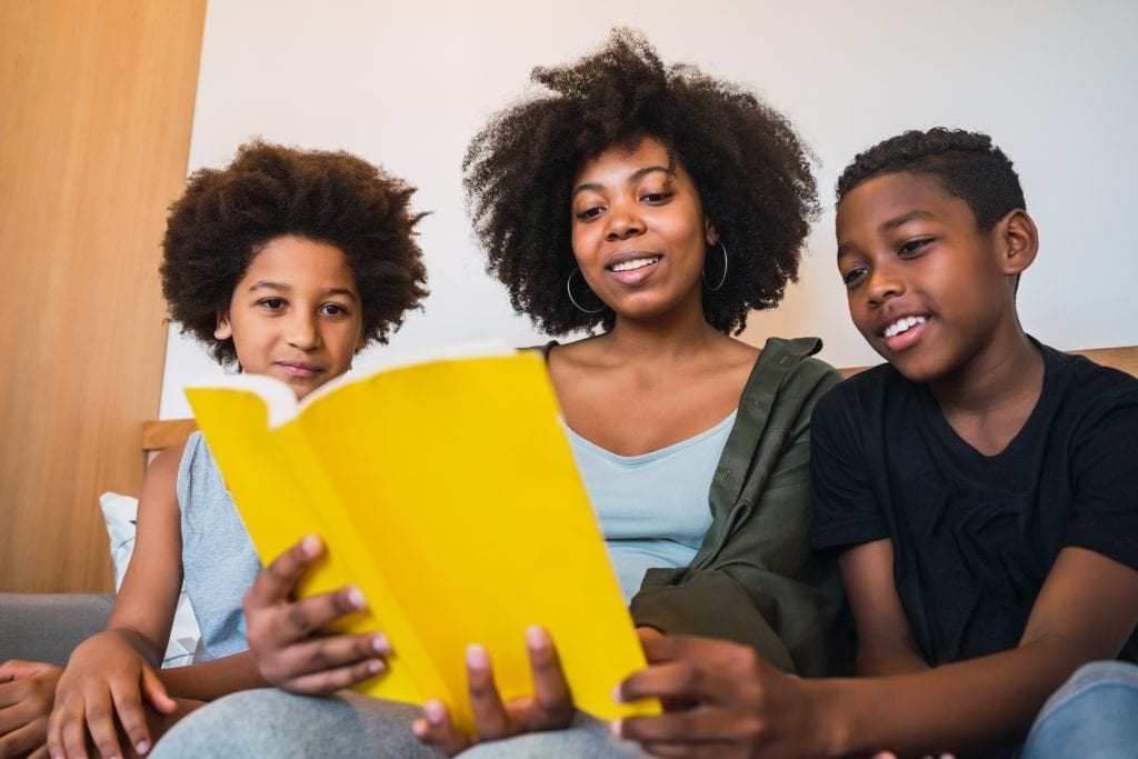 3 livros sobre ansiedade e solidão; mulher segurando um livro de capa amarela e lendo para duas crianças
