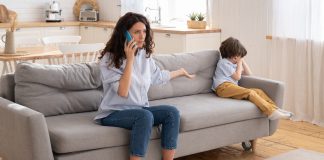 6 práticas comuns de alienação parental na pandemia; mãe sentada no sofá fala ao telefone e tem braço esticado para o lado com palma da mão para cima, n canto do sofá criança está sentada encolhida