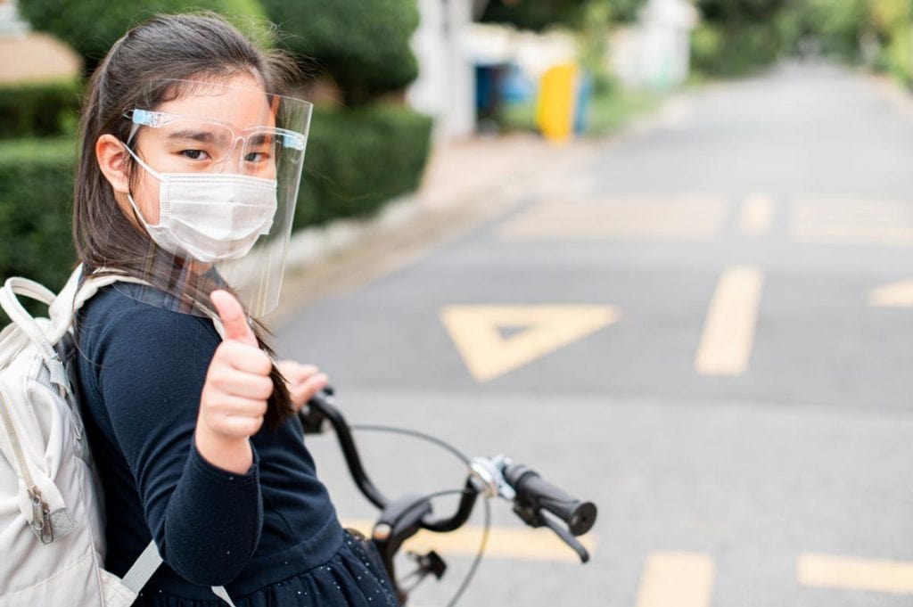 Liberdade sobre rodas: andar de bicicleta ganha mais relevância na pandemia; menina andando de bicicleta com máscara e face-shield