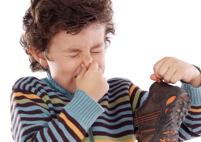 Criança com chulé: saiba como diminuir o mau cheiro nos pés; menino de olhos fechados aperta nariz com os dedos e segura um sapato na outra mão