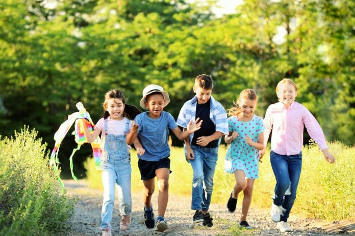 A busca pela saúde das crianças tem prescrição: mais contato com a natureza; 5 crianças caminham lado a lado em área verde ao ar livre