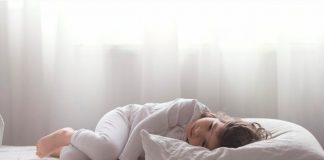 Distúrbios de sono de crianças autistas aumentam durante a pandemia; menina deitada na cama está encolhida e de olhos abertos