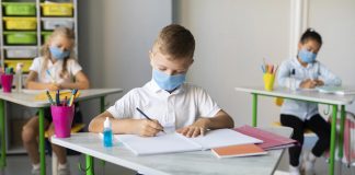 Escolas particulares perdem um terço das matrículas na pandemia; três alunos com máscaras sentados em carteiras escolares escrevem em cadernos