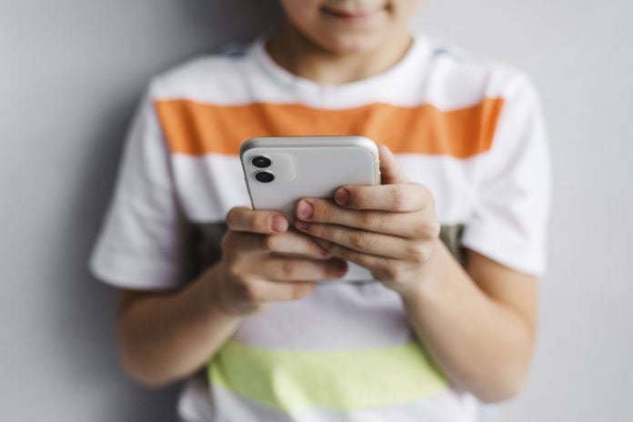 Crianças e celular: o que considerar antes de comprar o aparelho para o filho; criança segundo celular com as duas mãos