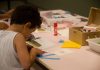 MAM oferece atividades educativas online em maio; criança de costas desenhando sobre mesa