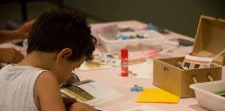 MAM oferece atividades educativas online em maio; criança de costas desenhando sobre mesa