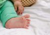 Sancionada lei que amplia doenças rastreadas no teste do pezinho pelo SUS; imagem mostra mão e pé de bebê que usa calca verde