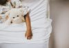 Xixi na cama: dicas para ajudar a criança; criança deitada na cama segurando um ursinho
