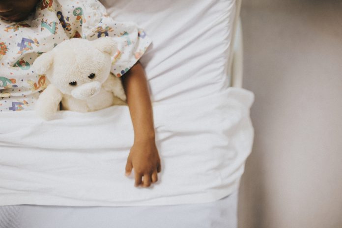 Xixi na cama: dicas para ajudar a criança; criança deitada na cama segurando um ursinho
