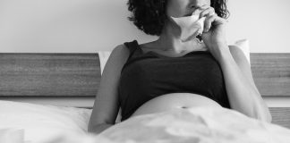 Depressão pós-parto - agora chamado perinatal, visto que se inicia durante a concepção do bebê - traz medos, dificuldades e incertezas; mulher grávida deitada na cama segura lencinho com a mão perto do nariz