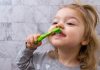 Os desafios de escovar bem os dentes das crianças; menina escova os dentes da frente com escova verde