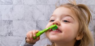 Os desafios de escovar bem os dentes das crianças; menina escova os dentes da frente com escova verde