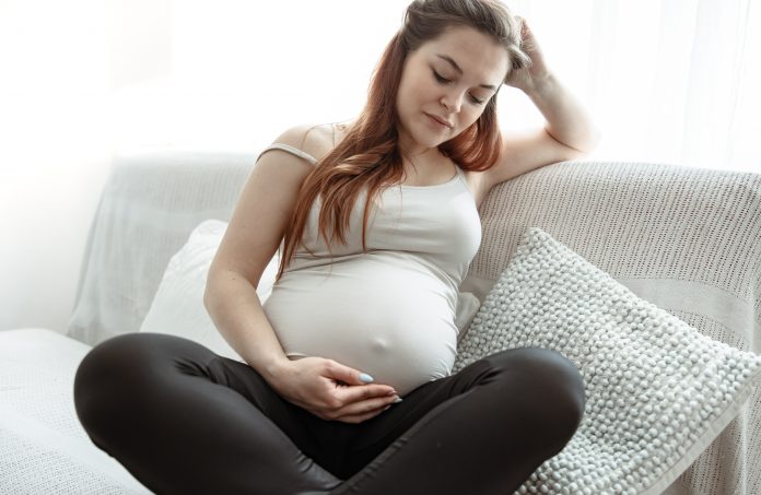 Mães na pandemia: precisamos despertar empatia por essas mulheres; mulher grávida sentada no sofá olhando para a barriga