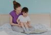 O que fazer para seu filho dormir sozinho no quarto dele (e a noite toda, de preferência); mãe lê para filho que está sentado em seu colo na cama