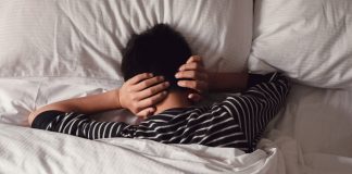 ‘Estresse tóxico’: 52% das crianças tiveram o sono prejudicado na pandemia; menino está deitado na cama de barriga para baixo e com mãos sobre a nuca