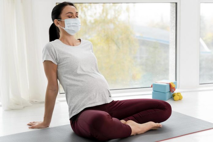 Grávidas sem comorbidades podem se vacinar contra Covid-19 em SP; grávida de máscara está sentada em colchonete