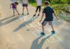 Brincadeiras populares para reviver a infância com os filhos; quatro crianças brincam de amarelinha desenhada no chão da rua com giz de cera