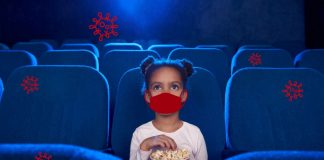 Cinema nas férias: dá para levar as crianças com segurança?; menina de máscara está sentada em poltrona de sala de cinema