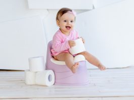 Desfralde: dicas para tirar a fralda do seu bebê (sem estresse); menina bebê de vestido rosa está sentada em piniquinho e segura rolo de papel de higiênico nas mãos