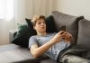O luto (diferente) dos adolescentes durante a pandemia; menino adolescente está deitado no sofá e olha para celular nas mãos