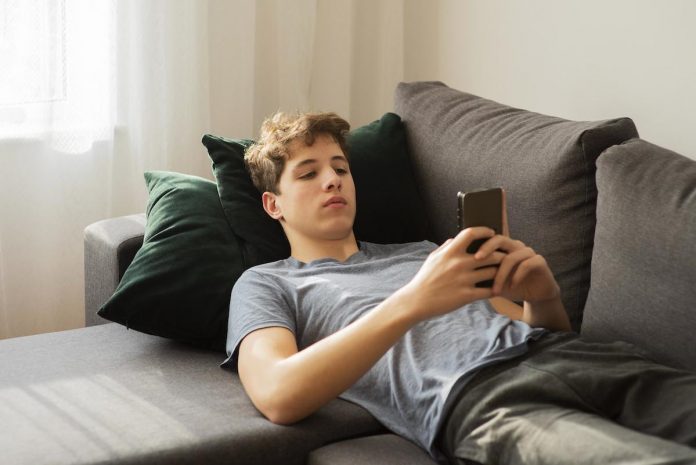 O luto (diferente) dos adolescentes durante a pandemia; menino adolescente está deitado no sofá e olha para celular nas mãos