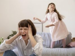 Os gritos dos pais: alguns dos motivos que levam a isso; mãe grita com mãos na cabeça e filha aparece ao fundo rindo