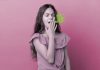 Criança com mau hálito: causas e formas de reduzir o cheiro forte na boca; menina de blusa rosa tem mão sobre boca aberta