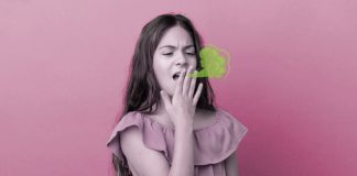 Criança com mau hálito: causas e formas de reduzir o cheiro forte na boca; menina de blusa rosa tem mão sobre boca aberta