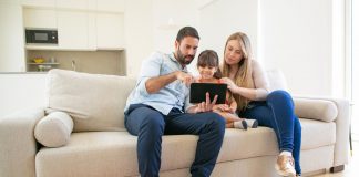 Gastos nas férias: 6 dicas para não estourar o orçamento da família; mãe, pai e filha olham para tela de ipad